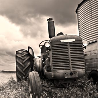 Black and white photo of a old tractor parked next to a short silo